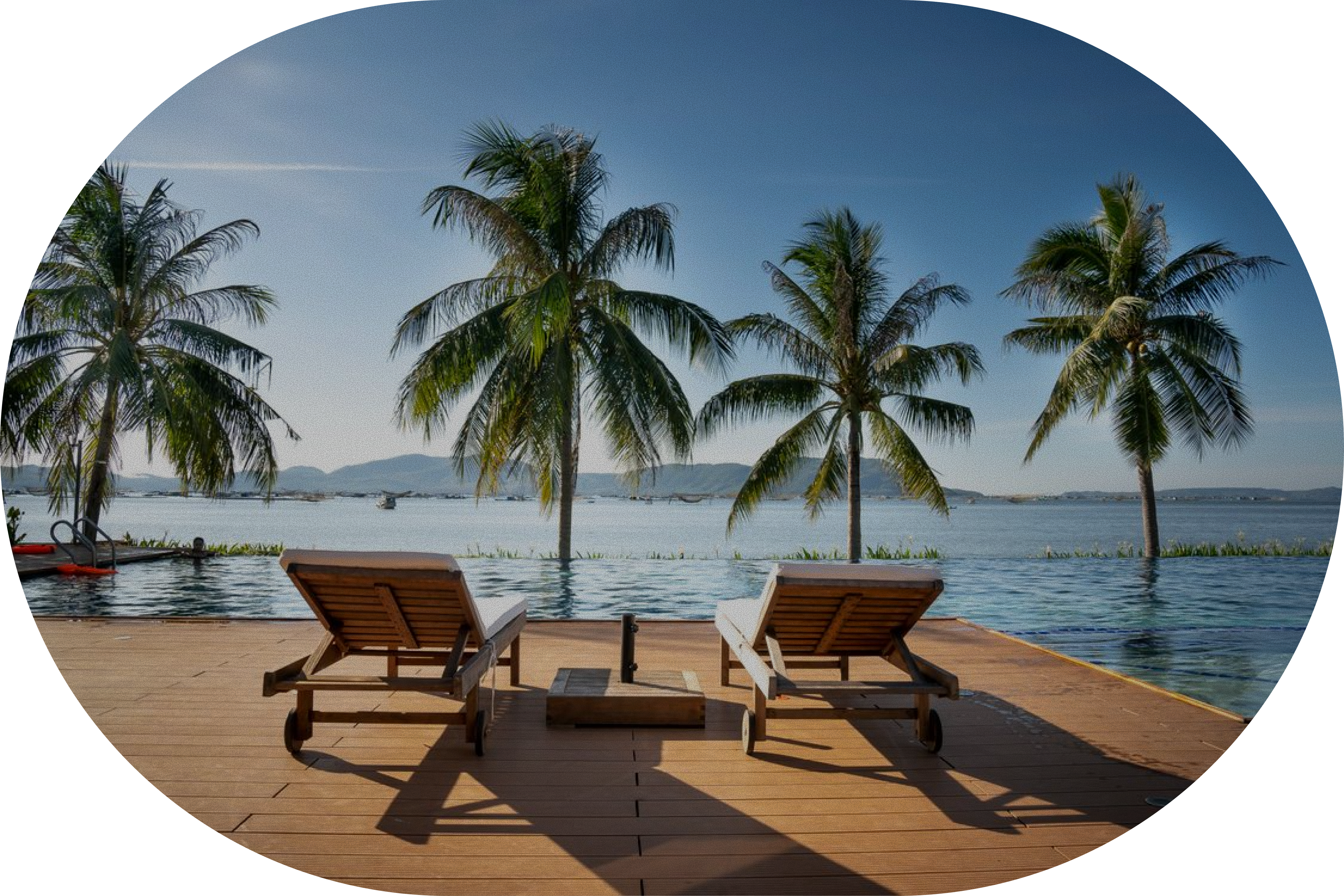 Wooden deck with two lounge chairs between palm trees, facing a calm lagoon